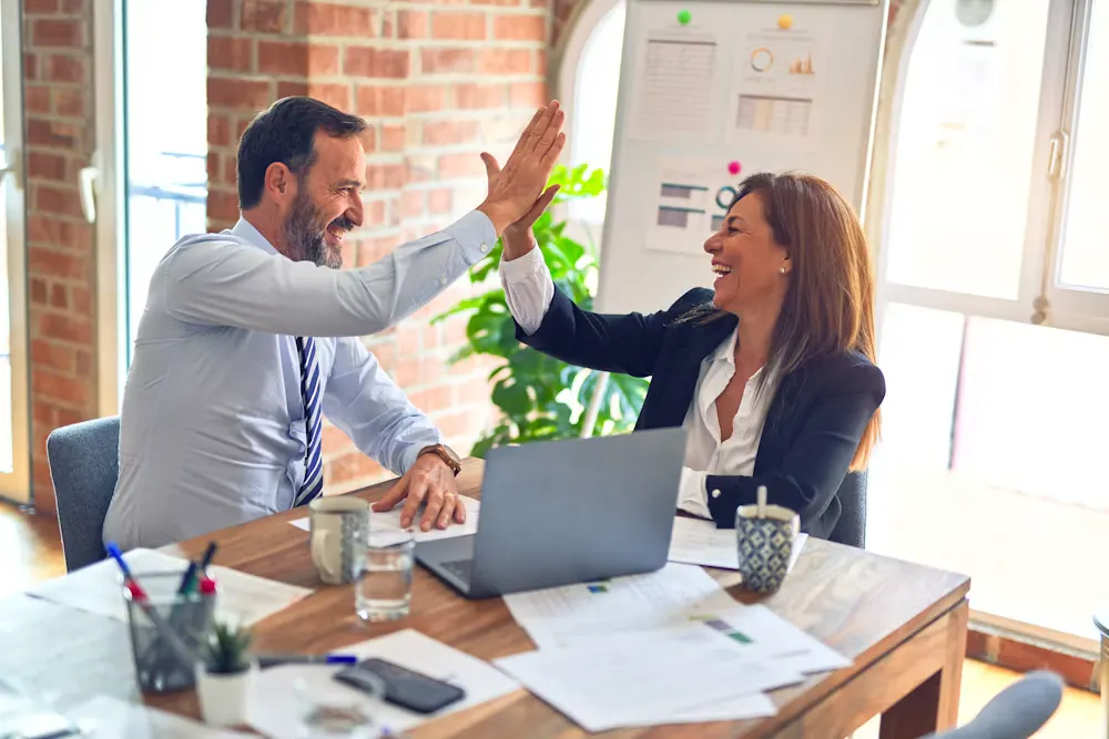 Two NS3 colleagues sharing a high-five at their desk